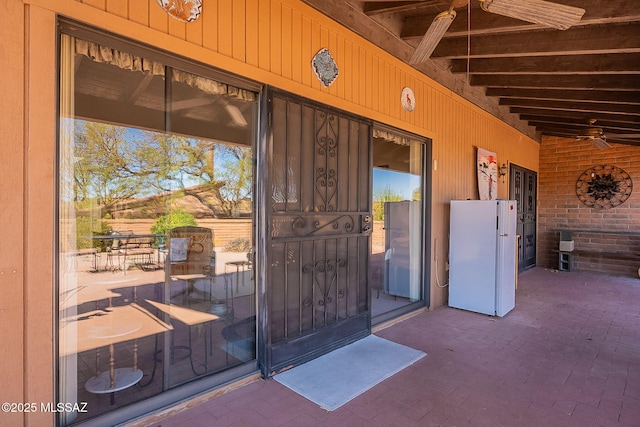 entrance to property featuring brick siding, ceiling fan, and a patio