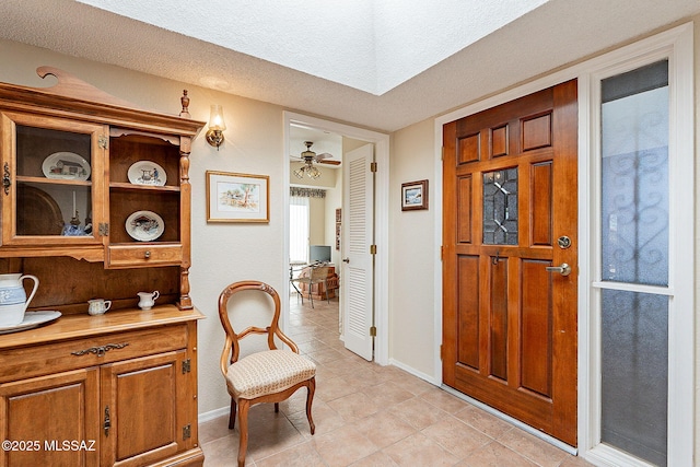 foyer with ceiling fan, a textured ceiling, baseboards, and light tile patterned floors