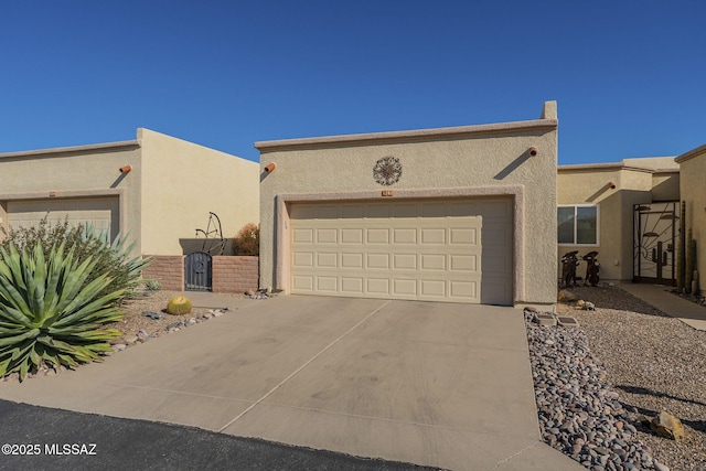 pueblo-style home with driveway, an attached garage, a gate, and stucco siding