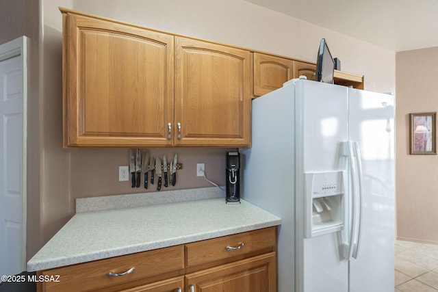 kitchen featuring brown cabinetry, white refrigerator with ice dispenser, light countertops, and light tile patterned floors