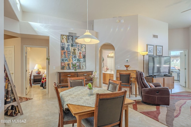 dining room featuring arched walkways, light tile patterned floors, a towering ceiling, and visible vents