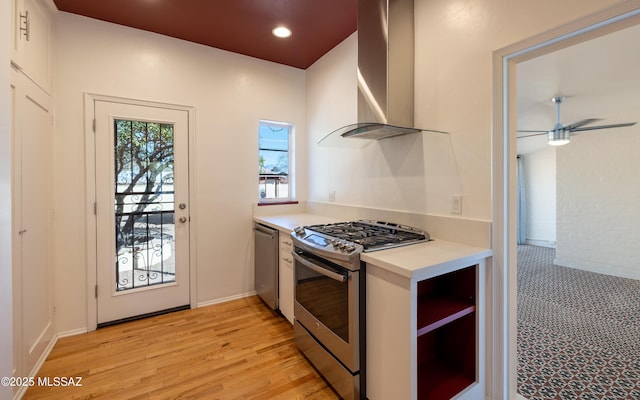 kitchen featuring stainless steel appliances, light countertops, a ceiling fan, light wood-type flooring, and wall chimney exhaust hood