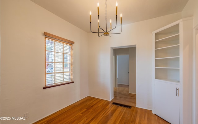 unfurnished room featuring built in features, washer / clothes dryer, visible vents, wood finished floors, and a chandelier