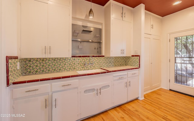 kitchen with tasteful backsplash, light wood-style floors, tile counters, and white cabinets