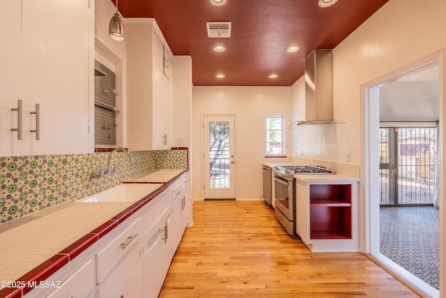 kitchen with light wood finished floors, visible vents, gas stove, a sink, and wall chimney exhaust hood