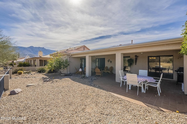 rear view of property with stucco siding, a mountain view, outdoor dining area, and a patio