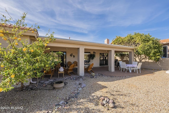 rear view of property featuring a patio, a chimney, fence, and stucco siding