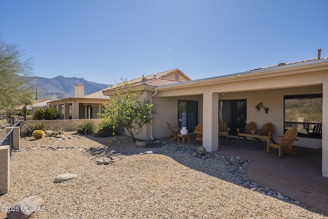 rear view of property featuring a patio, a tile roof, a mountain view, and stucco siding