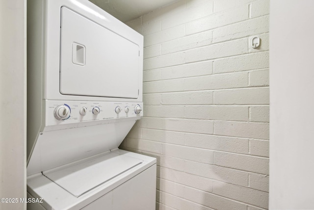 clothes washing area with concrete block wall, laundry area, and stacked washer / dryer