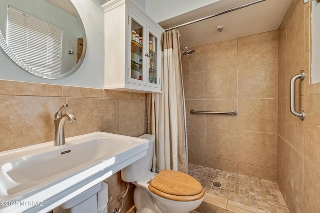 bathroom featuring a sink, tiled shower, toilet, and tile walls