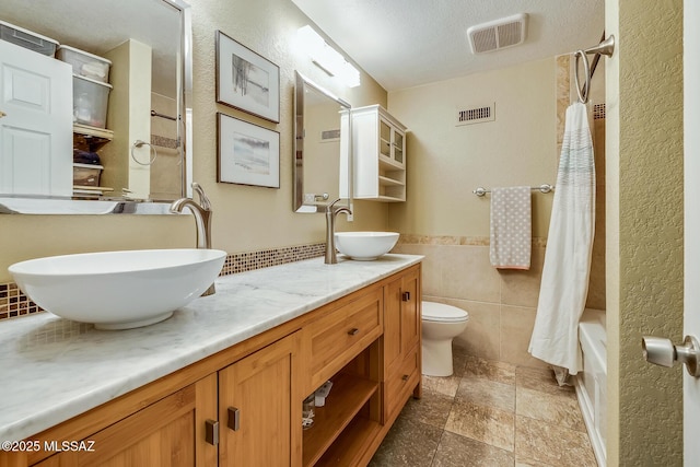 bathroom with a sink, visible vents, and tile walls