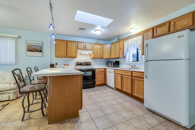 kitchen with a sink, under cabinet range hood, white appliances, a skylight, and light countertops