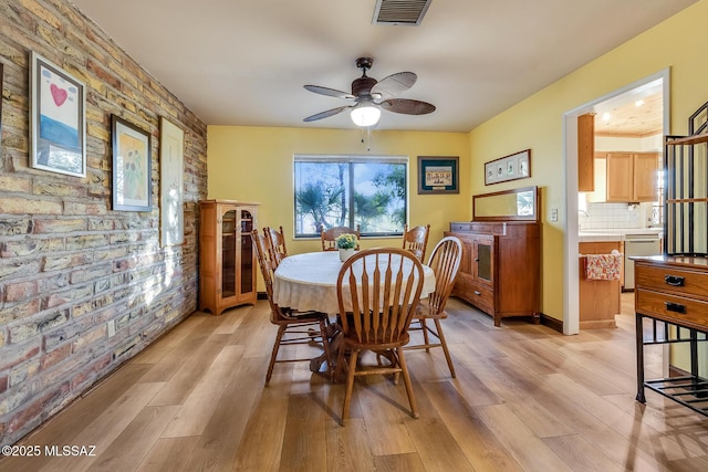 dining room featuring light wood-type flooring, visible vents, brick wall, and a ceiling fan