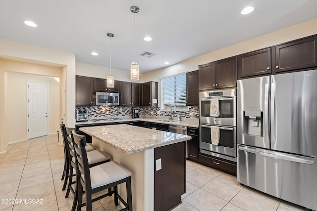 kitchen featuring dark brown cabinets, hanging light fixtures, stainless steel appliances, a center island, and light tile patterned floors