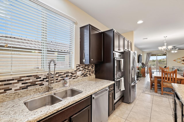 kitchen featuring appliances with stainless steel finishes, dark brown cabinetry, light stone counters, light tile patterned flooring, and sink