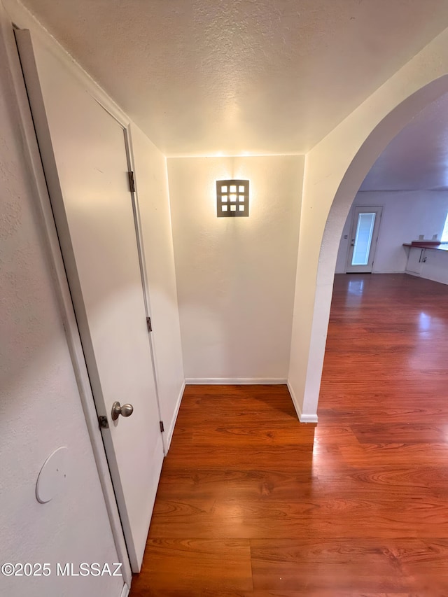 hall with arched walkways, a textured ceiling, wood finished floors, and baseboards