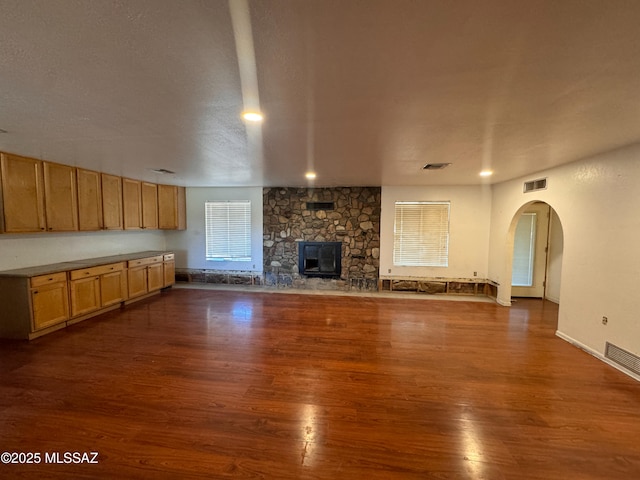 unfurnished living room with visible vents, arched walkways, and dark wood-type flooring