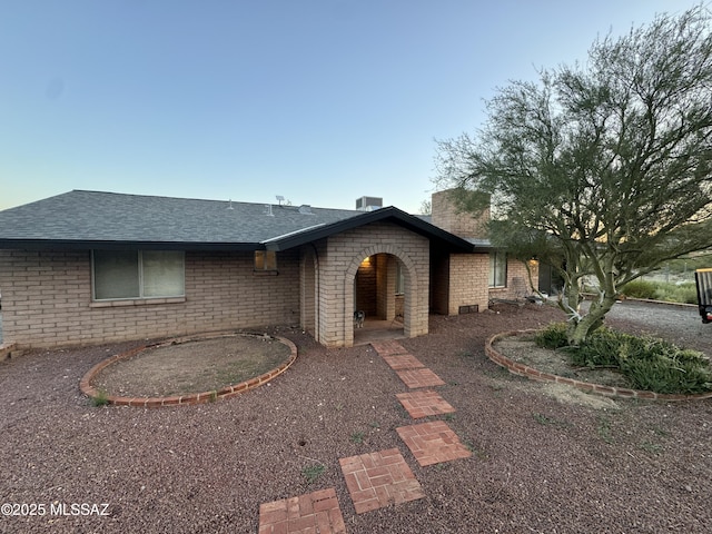 ranch-style home with central air condition unit, brick siding, a patio area, and roof with shingles