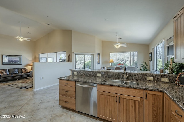 kitchen with a sink, open floor plan, stainless steel dishwasher, brown cabinets, and dark stone counters