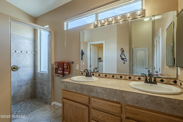 bathroom with double vanity, a tile shower, a sink, and tile patterned floors
