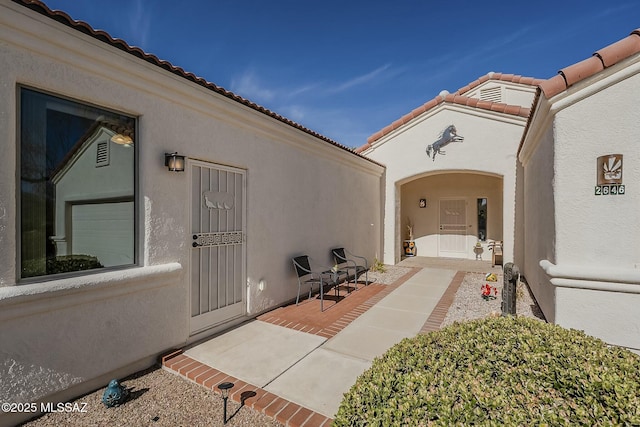 property entrance with a patio, a tile roof, and stucco siding