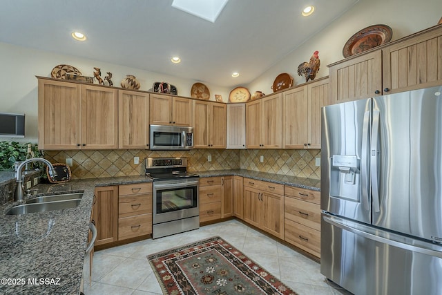 kitchen featuring dark stone counters, stainless steel appliances, backsplash, and a sink