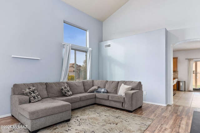 living room featuring light wood finished floors, baseboards, arched walkways, and high vaulted ceiling