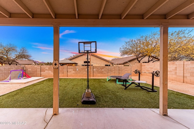 patio terrace at dusk featuring a fenced backyard and a yard