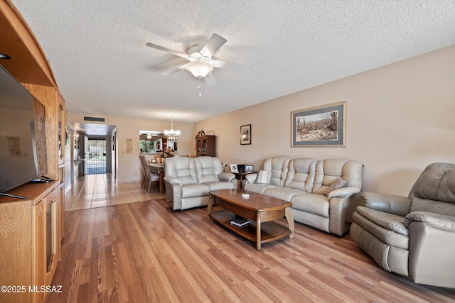 living room with ceiling fan with notable chandelier, light hardwood / wood-style floors, and a textured ceiling