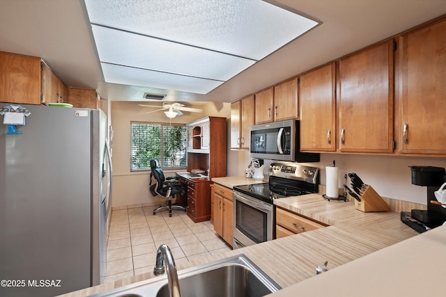 kitchen with appliances with stainless steel finishes, light tile patterned floors, sink, and ceiling fan