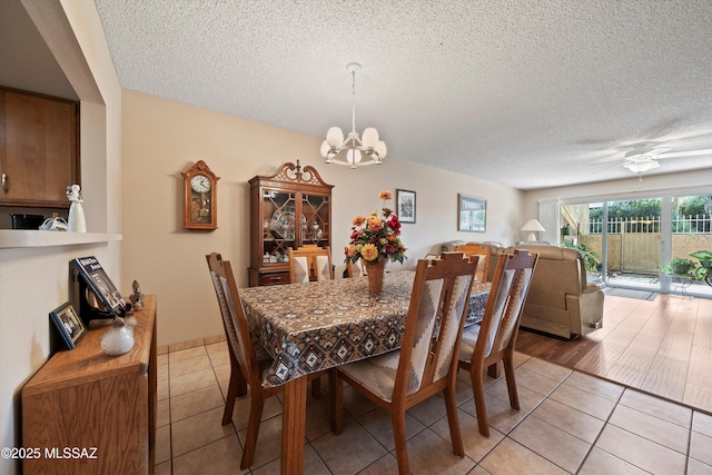 tiled dining space with a textured ceiling and ceiling fan with notable chandelier