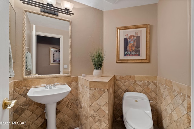 bathroom with a wainscoted wall, a sink, tile walls, and toilet