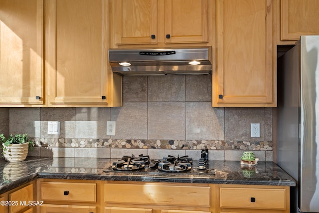 kitchen with black gas cooktop, under cabinet range hood, freestanding refrigerator, decorative backsplash, and dark countertops