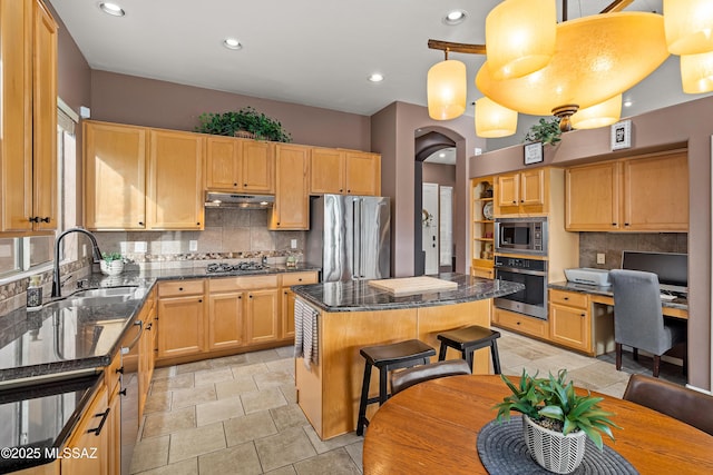 kitchen with under cabinet range hood, stainless steel appliances, a kitchen island, a sink, and decorative backsplash