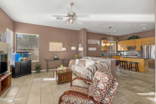 living area featuring light tile patterned flooring, visible vents, baseboards, and ceiling fan with notable chandelier