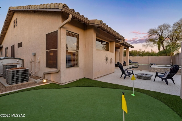 back of property at dusk featuring stucco siding, an outdoor fire pit, a patio area, fence, and cooling unit