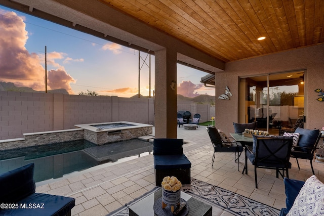 patio terrace at dusk with an outdoor fire pit, a fenced backyard, a jacuzzi, a fenced in pool, and outdoor dining space