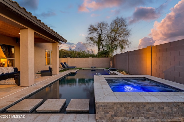 pool at dusk with an in ground hot tub, a fenced backyard, a fenced in pool, and a patio