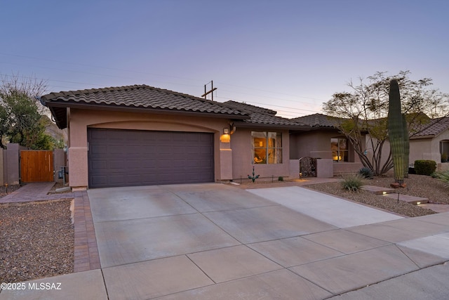 view of front facade featuring driveway, a tiled roof, an attached garage, fence, and stucco siding