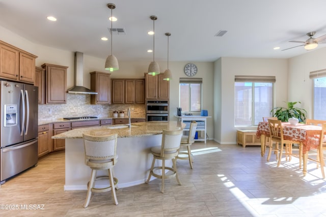 kitchen with visible vents, a sink, stainless steel appliances, wall chimney range hood, and backsplash