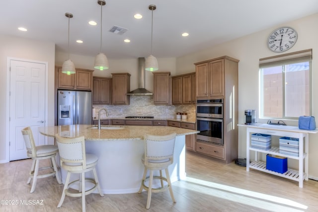 kitchen with visible vents, wall chimney exhaust hood, appliances with stainless steel finishes, a sink, and backsplash