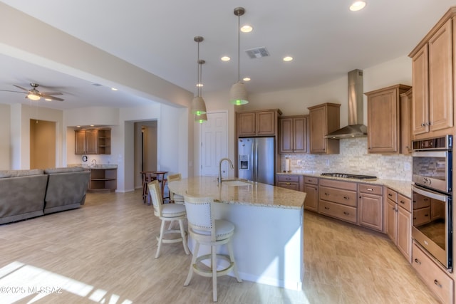 kitchen featuring stainless steel appliances, tasteful backsplash, visible vents, a sink, and wall chimney exhaust hood