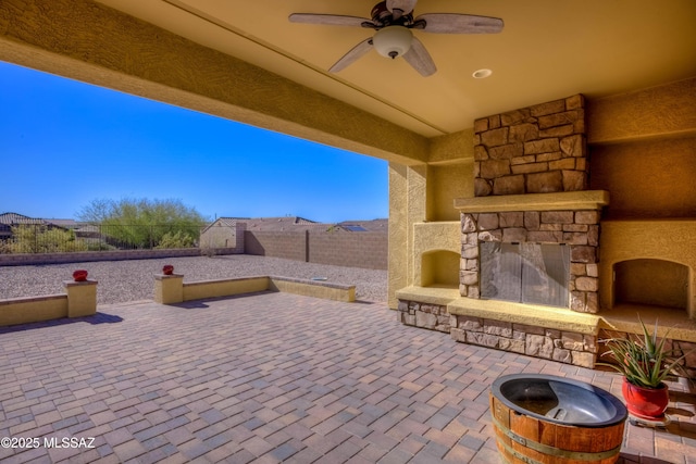 view of patio featuring a fenced backyard, an outdoor stone fireplace, and ceiling fan