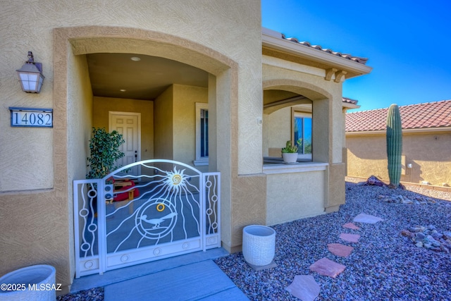 entrance to property featuring fence, a tiled roof, and stucco siding