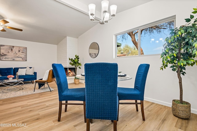 dining room with a multi sided fireplace, vaulted ceiling, wood finished floors, baseboards, and ceiling fan with notable chandelier