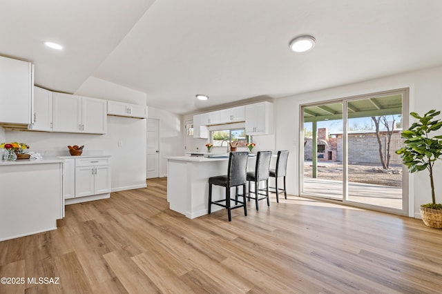 kitchen with light wood-style floors, white cabinetry, light countertops, and a breakfast bar area