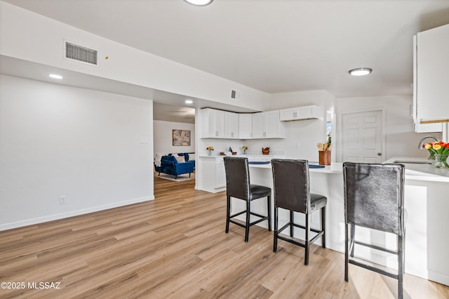 kitchen with a sink, visible vents, white cabinetry, a kitchen breakfast bar, and light countertops