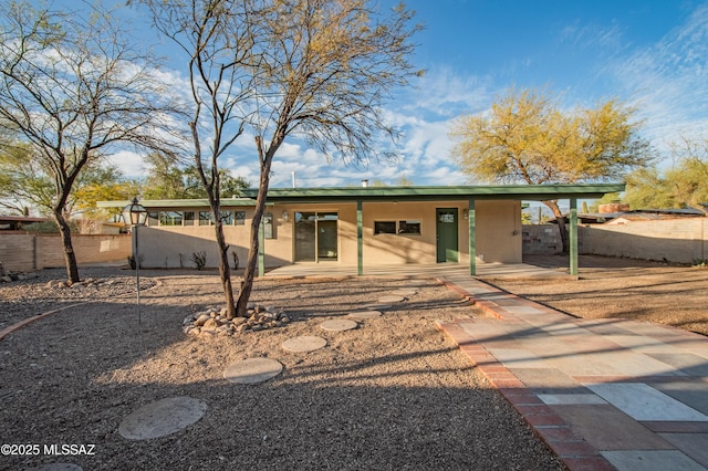 rear view of house with a patio area, fence, and stucco siding