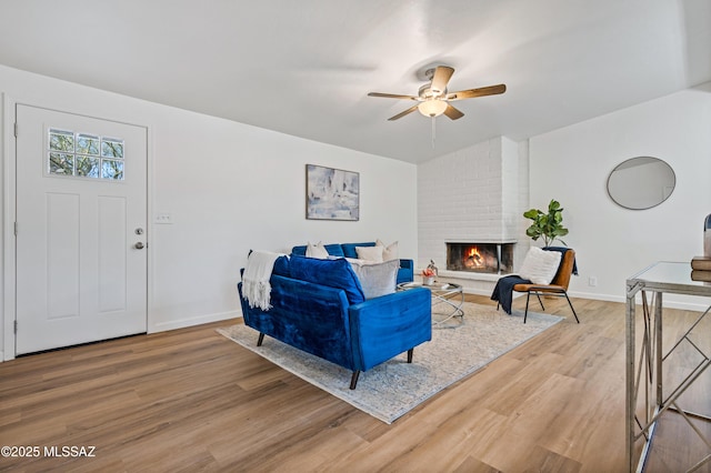 living room with ceiling fan, a brick fireplace, wood finished floors, and baseboards