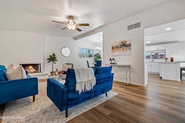 living area with visible vents, lofted ceiling with beams, a brick fireplace, light wood-type flooring, and baseboards